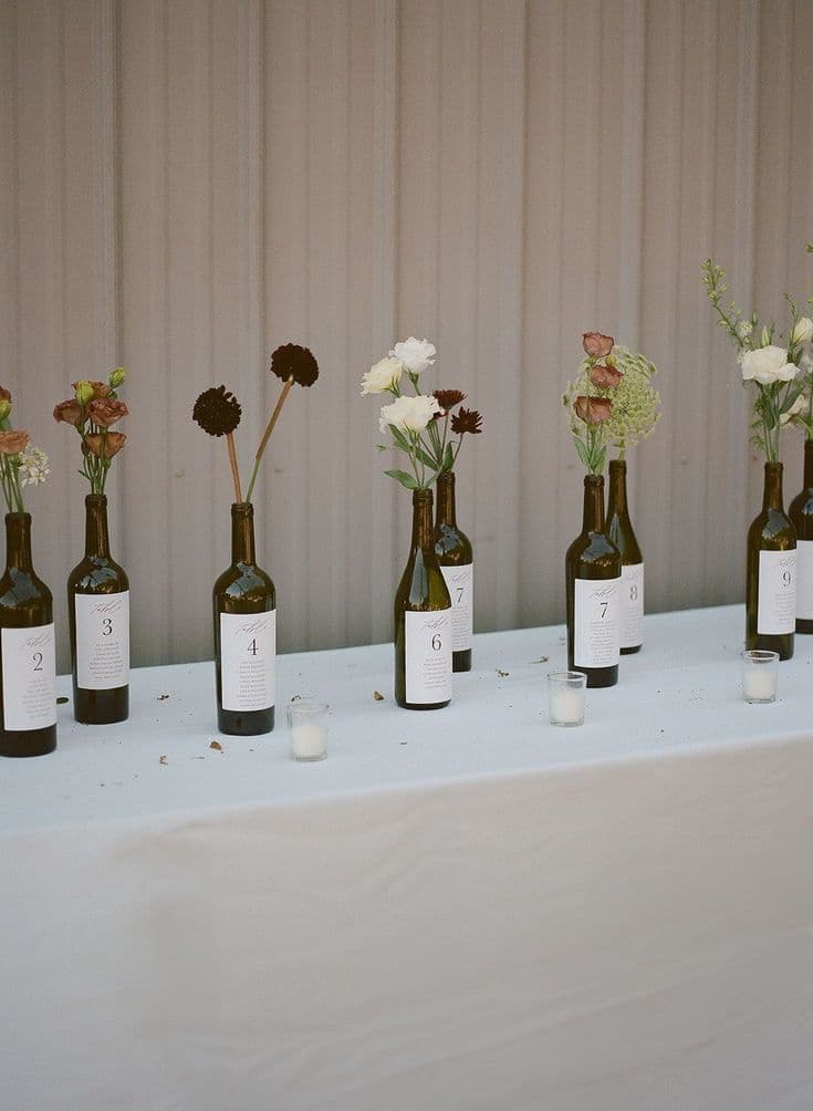 Wine bottles used as table numbers, each holding a single stem