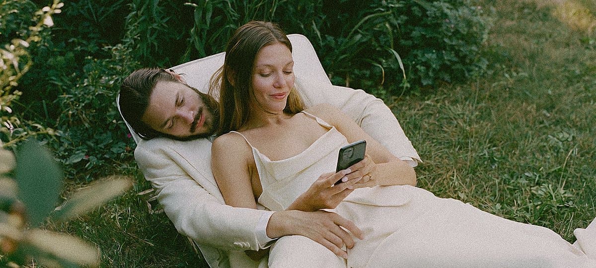 A couple lying in the grass, one of them holding a phone