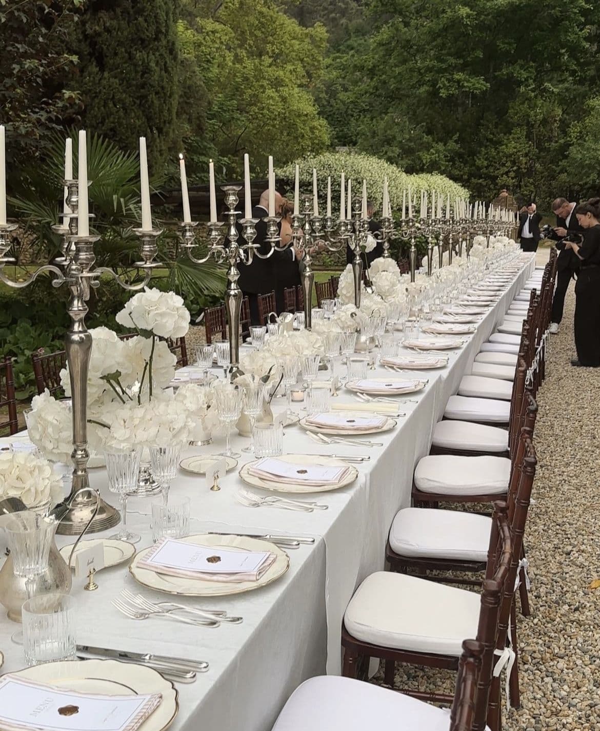A long garden table set with silver candelabra and low white florals