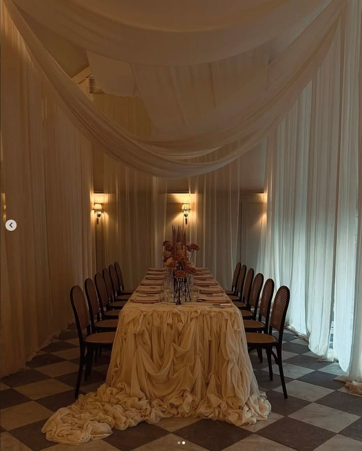 A draped dining room lit by wall sconces and low candlelight