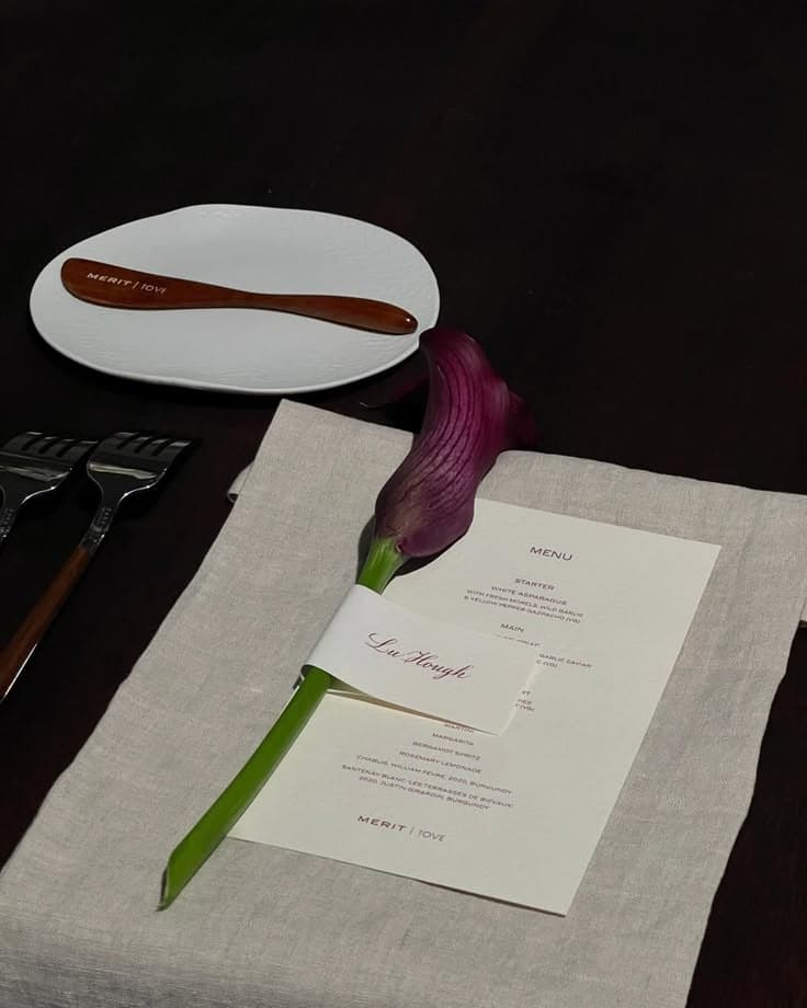 A candlelit place setting — a printed menu and a calla lily on linen
