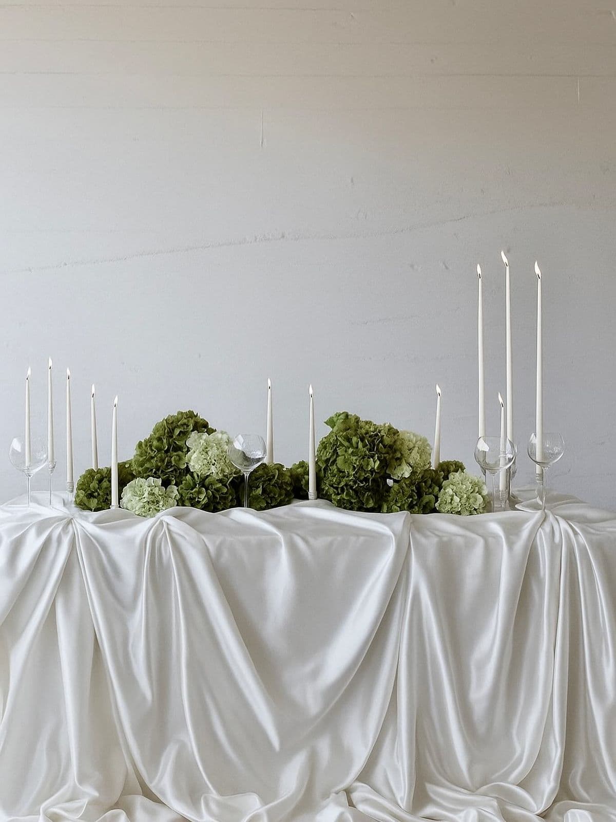 A draped silk table with green hydrangea and tall tapers in low light