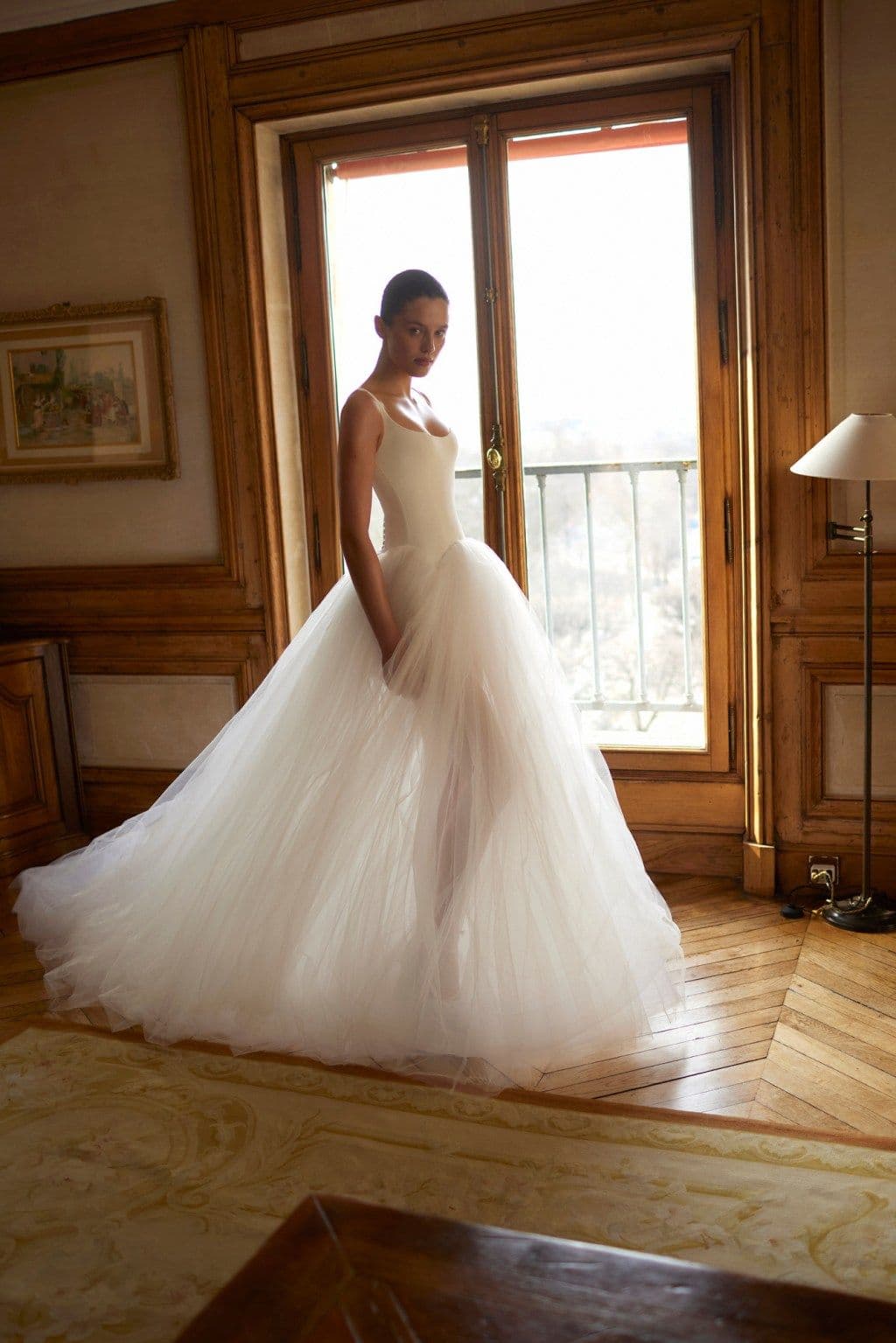 A bride in a full tulle gown standing by a panelled window