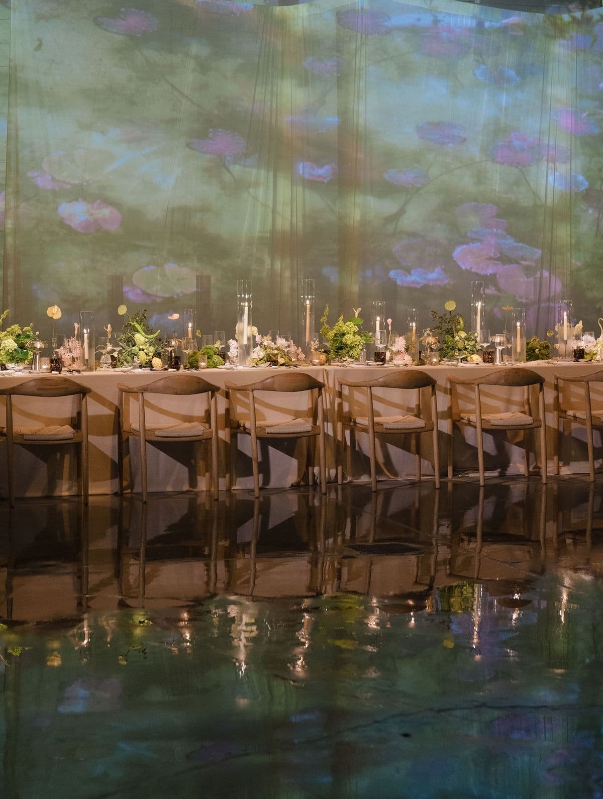 A dinner beneath a Monet water-lily projection, mirrored in a glassy floor