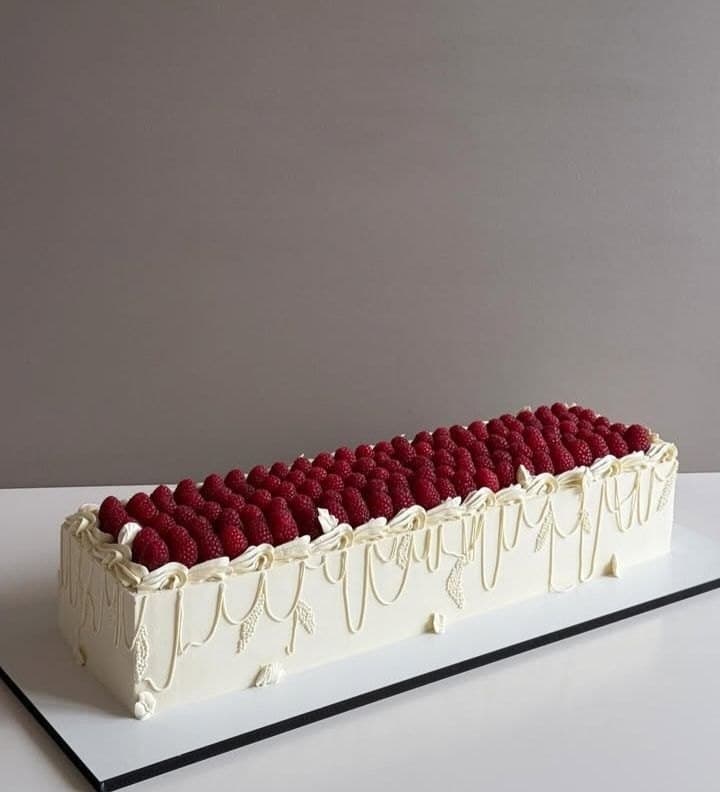 A long rectangular white wedding cake with piped lambeth swags, topped with rows of fresh raspberries