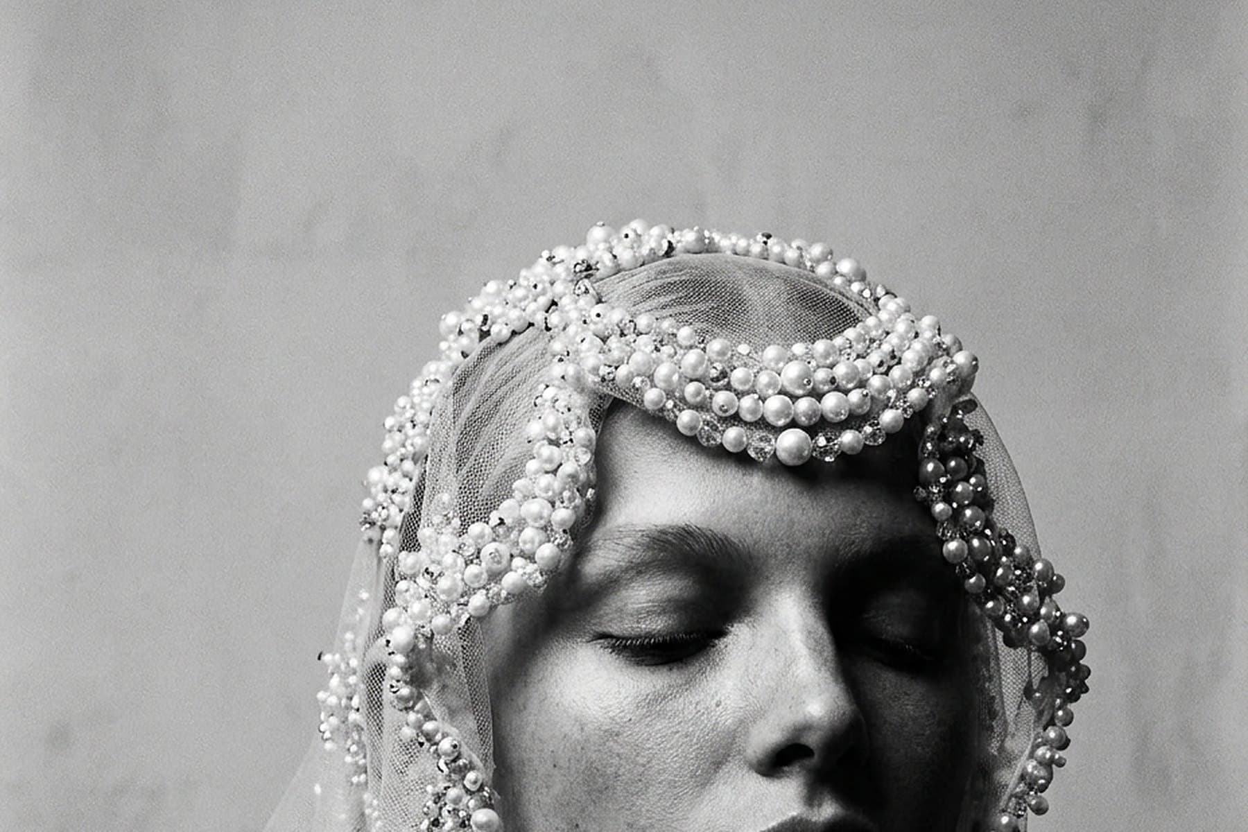 A bride in a beaded pearl headpiece and veil, eyes closed, photographed in black and white