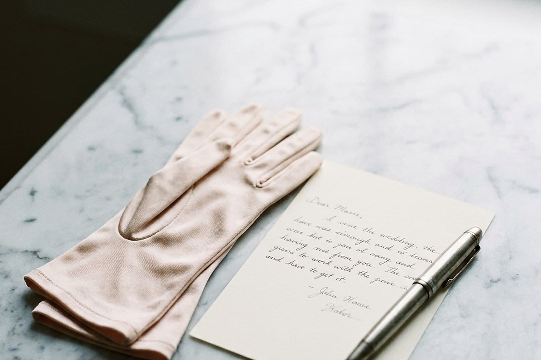 A handwritten letter, a pen and a pair of gloves on a marble table