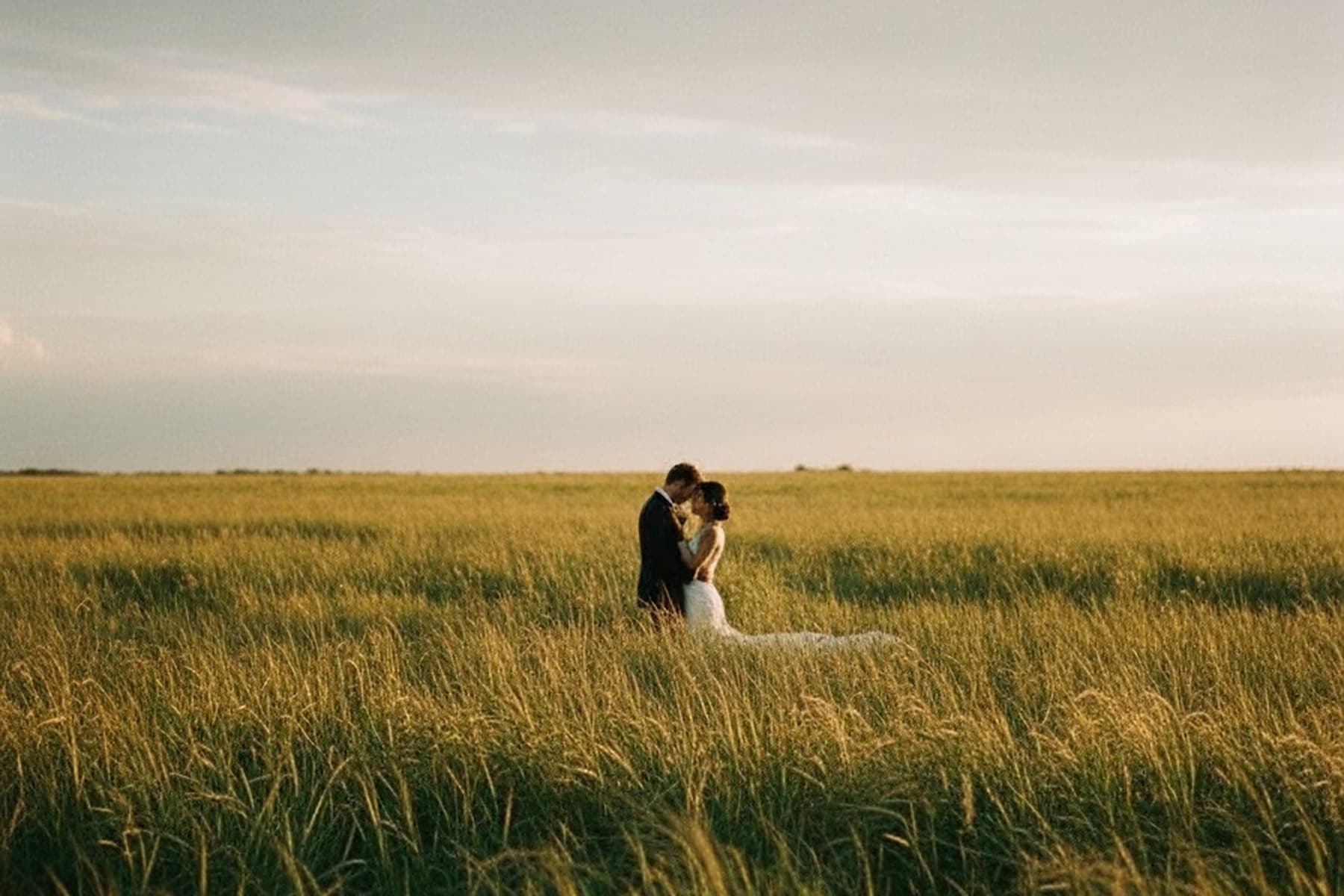 A couple standing together in a wide golden field at dusk